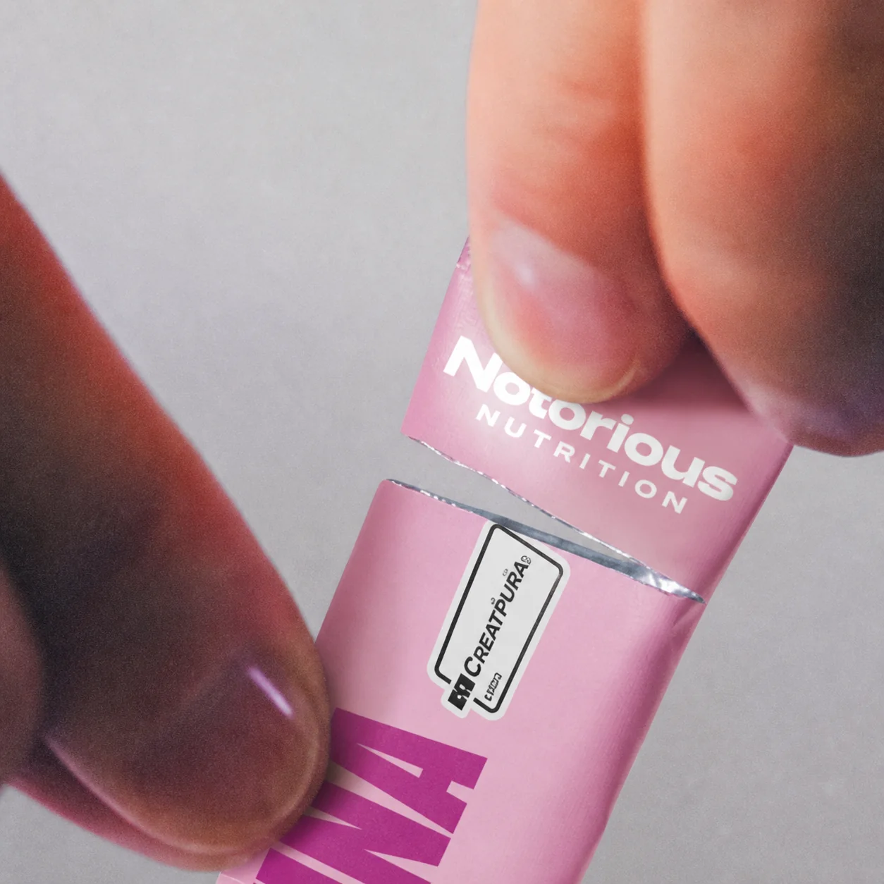 Mãos abrindo um sachê rosa de creatina Notorious Nutrition