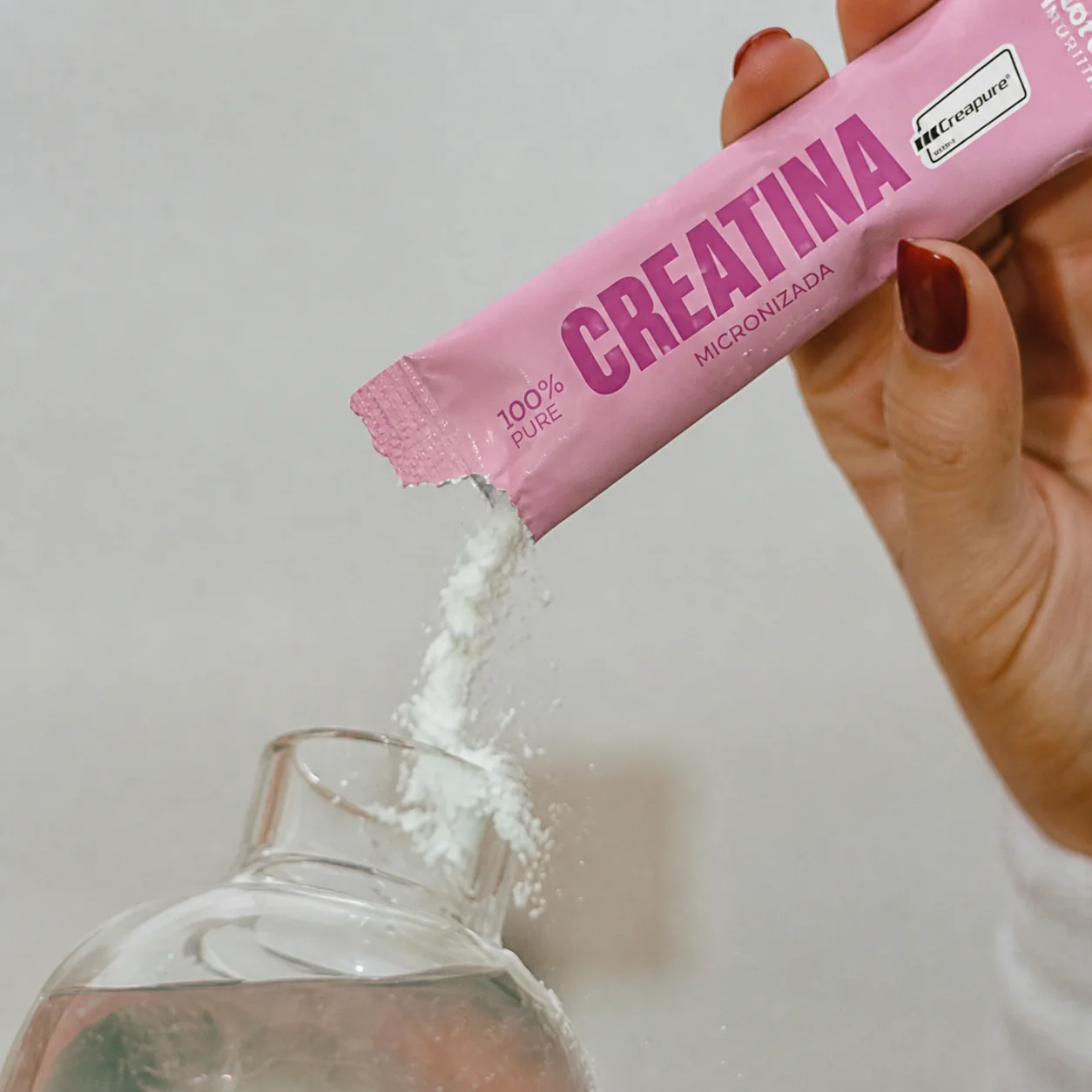 Creatina sendo despejada de um sachê rosa em um copo